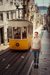 Young smiling woman tourist standing near the  retro yellow tram on the street in Lisbon city,...