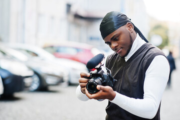 Young professional african american videographer holding professional camera with pro equipment. Afro cameraman wearing black duraq making a videos.
