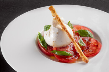 Burrata cheese and tomato salad with Basil and olive oil served on a white plate
