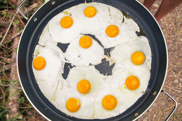 Multiple fried eggs in a frying pan outdoors.