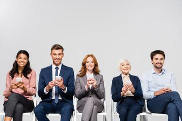 Smiling multicultural businesspeople using smartphones isolated on grey