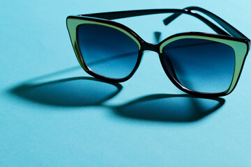 Sunglasses close up. The shadow from the glasses falls on the blue surface. Horizontal, free space on the left.