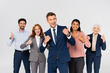 Fototapeta na wymiar Cheerful multiethnic businesspeople showing like gesture isolated on grey