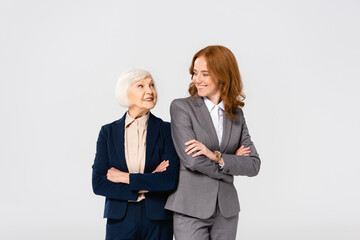 Businesswoman looking at senior colleague with crossed arms isolated on grey