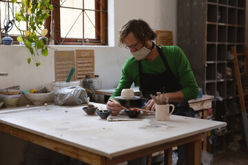 Caucasian male potter in face mask working in pottery studio