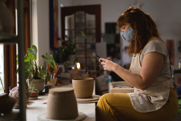 Caucasian female potter in face mask working in pottery studio
