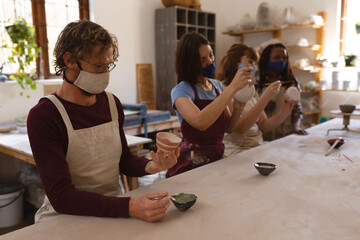 Multi-ethnic group of potters in face masks working in pottery studio