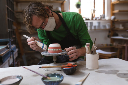Caucasian male potter in face mask working in pottery studio