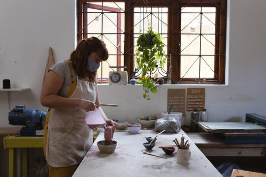 Caucasian female potter in face mask working in pottery studio