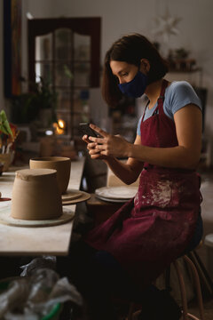 Caucasian female potter in face mask working in pottery studio