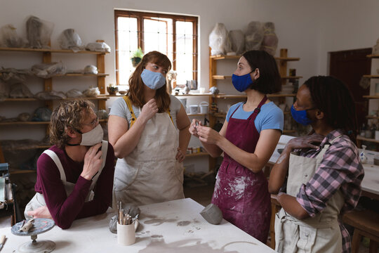 Multi-ethnic group of potters in face masks working in pottery studio