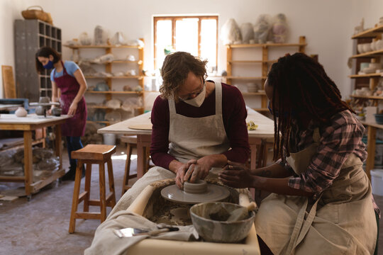 Caucasian male and mixed race female potters in face masks working in pottery studio