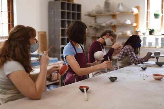 Multi-ethnic group of potters in face masks working in pottery studio
