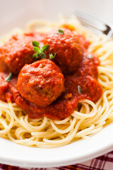 Italian meatballs with tomato sauce, on a bed of spaghetti on a white plate. Selective focus - shallow depth of field.