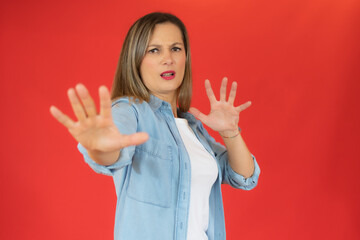 Young woman wearing denim shirt standing over isolated red background Moving away hands palms showing refusal and denial with afraid and disgusting expression. Stop and forbidden.