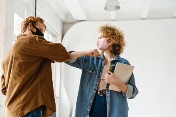 Young happy friends in face masks elbow bumping at meeting