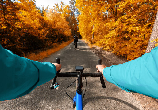 First-person view of a cyclist riding with a friend in the autumn forest with yellow leaves.