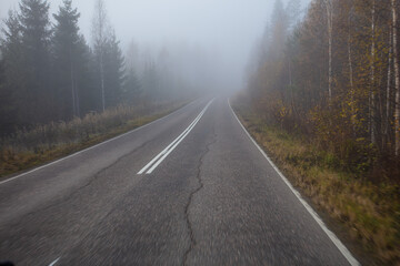 Poor visibility. The road is in heavy fog, along the edges of the road there is a forest. Autumn morning in November. Photo through the windshield of a car