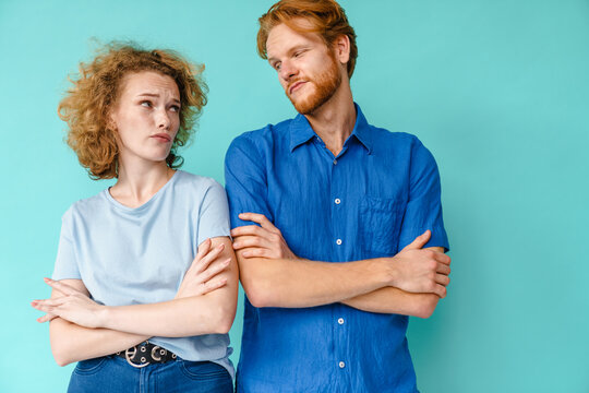 Confused Couple Looking At Each Other While Posing With Arms Crossed