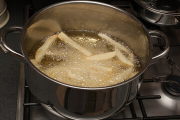 Homemade potato chips frying in a pan of hot oil