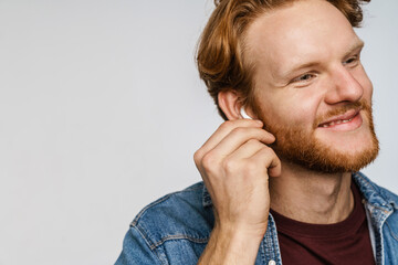Joyful redhead guy in wireless earphones smiling at camera