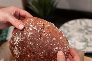 Round homemade rye bread in female hands on the background of the kitchen. Homemade bread baking.