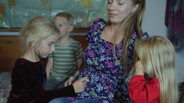 Children listen to their pregnant mother's belly with a stethoscope.