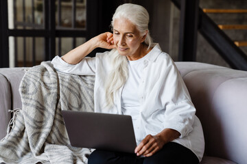 Obraz premium Retired senior woman sitting at home using laptopn a couch