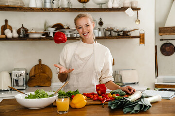 Beautiful woman smiling and flipping bell pepper while making lunch - Powered by Adobe