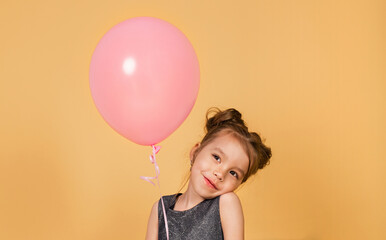 Fototapeta na wymiar Little beautiful girl with a big pink balloon in her hands makes a wish. Portrait cute birthday kid. Smiling four five year old child. Isolated orange background. Happy childhood concept