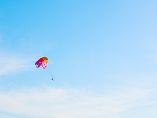 Fototapeta na wymiar Man on multicolor parachute on zipline in blue sky