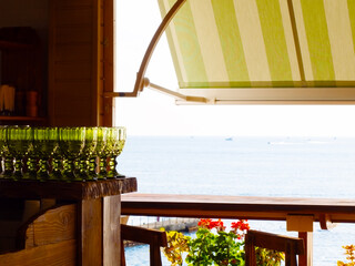 Fragment of an open-air cafe with many green glasses on the bar, a fabric visor and a sea view