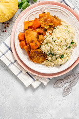Chicken stew with pumpkin, carrots, tomatoes, spices and garlic, served with couscous on a ceramic plate. Moroccan food, Maghreb cuisine. Chicken with vegetables and couscous on a gray table top view