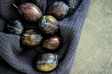 Plums on textured blue kitchen towel. Fresh summer fruits top view photo. Healthy eating concept. 