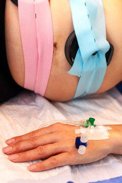 Gro&szlig;aufnahme eines Babybauchs mit angelegtem CTG und Venenkatheter in der Hand