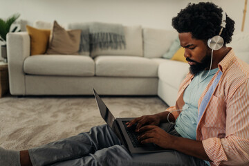 Young black man with earphones sitting on the floor and using laptop