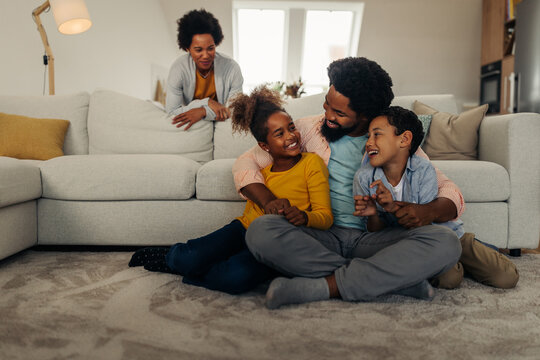 Afro parents and their children are socializing while sitting on the sofa in the living room