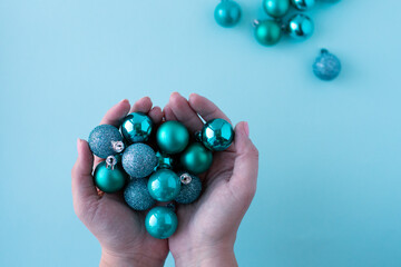 Female hands holding Christmas ornaments. Baubles are turquoise and small. Tiffany color new year background