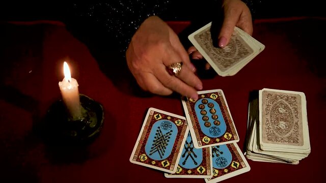 A woman reads Tarot cards by candlelight on a red table
