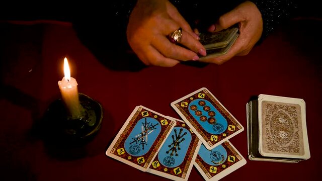 A woman reads Tarot cards by candlelight on a red table
