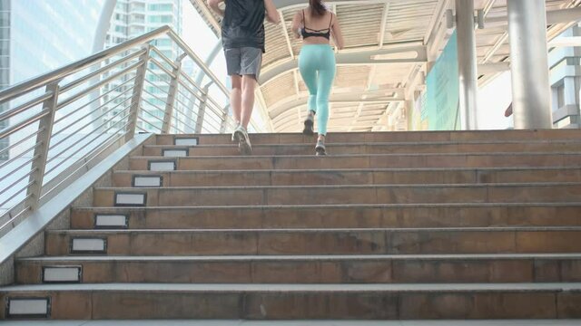Couple Asian sport man and woman are jogging and pass the stairs in big city. Concept of healthy lifestyle in main town with take care by exercise.