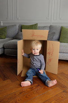 Toddler boy sitting in cardboard box holding marker