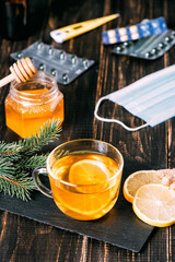 Glass cup of hot ginger tea with lemon and honey on dark wooden table. Sliced lemons and pills on stone board