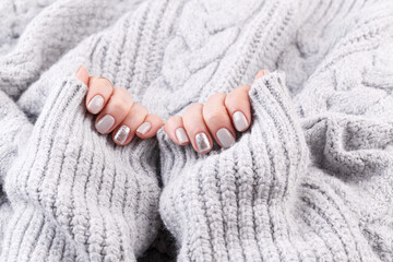 Manicured woman hands, grey knitted background, close up