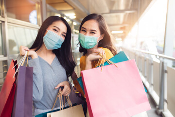 Asian woman wearing face mask. Happy woman with shopping bags enjoying in shopping. Girl holding colour paper bag.Friends walking in shopping mall.time shopping coronavirus crisis or covid19 outbreak.