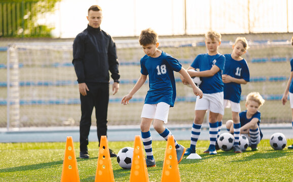 Group of Young Boys on Football Training. School Kids with Soccer Coach Teacher. Child Running with Sports Ball Towards Training Cones. Boys Training Technique at Summer Soccer Camp