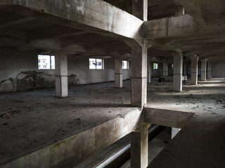 Fototapeta premium Interior of an old abandoned concrete hall. Empty messy industrial warehouse with several floors and a hole in the floor.