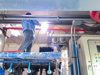 mechanic standing on a scaffold welding pipes to repair the sprinkler system in the pump room.