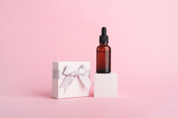 Serum glass bottle with pipette on the white cube and white gift box with silver ribbon bow near on...
