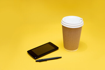 Empty craft glass, telephone and ballpoint pen on yellow background.